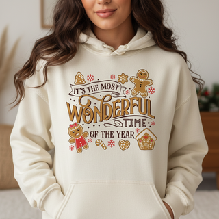 Person wearing a cream hoodie with festive text and gingerbread graphics. It's the most wonderful time of the year