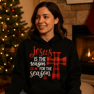 Woman wearing a hoodie with a Christmas message in front of a decorated tree and fireplace. Jesus is the reason for the season on a black hoodie