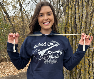 This is a Raised On Country Music Graphic Hoodie on a solid navy. The brand is Next Level.