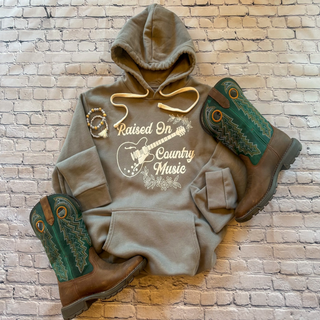 This is a Raised On Country Music Graphic Hoodie and the color is solid stone. The brand is Next Level and is presented as a flat lay.