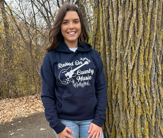This is a Raised On Country Music Graphic Hoodie on a solid navy. The brand is Next Level.